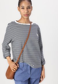 Black and white striped long-sleeve top with a round neckline, paired with light blue trousers. A brown crossbody bag is worn over the shoulder.