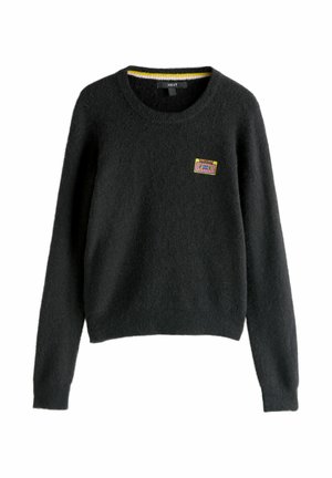 Czarny, puszysty sweter z długimi rękawami, okrągłym dekoltem i małą kolorową naszywką w kształcie kasety na lewej piersi, wiszący na tle białym.