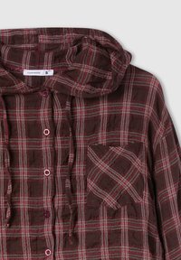 Camicia flanella a quadri di un intenso bordeaux scuro con linee bianche e rosse. Dotata di cappuccio, chiusura con bottoni e tasca sul petto. Tessuto morbido e texturizzato.