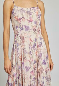 Bloemendress van lichtgewicht stof met een getailleerde bustier, dunne bandjes en een vloeiende, geplooide rok met pastel paarse en roze bloemen.