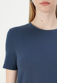 Sötétkék rövid ujjú póló kerek nyakkivágással, sima textúrával és diszkrét bordázott részletekkel a magokon és az alján.