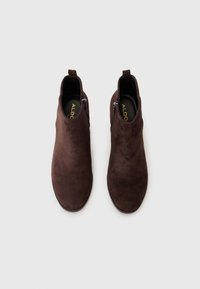 Stivaletti alla caviglia in suede marrone con una superficie liscia, cerniere laterali e un design minimalista. Suole piatte e un anello per indossarli facilmente.