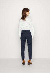 Jūras armijas stilāšūtas bikses ar slaidu piegriezumu, sānu un aizmugures kabatām. Valkā ar baltu garo piedurkņu krekliņu un brūnām bloku papēžu sandālēm.