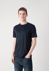 T-shirt blu navy in tessuto morbido con scollatura rotonda e maniche corte, abbinato a jeans in denim scuro. Design semplice e minimalista.