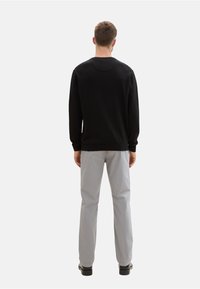 Schwarzer Sweatshirt mit Rundhalsausschnitt, gerippten Bündchen und Saum, kombiniert mit hellgrauen Hosen und schwarzen Schuhen, von hinten betrachtet.