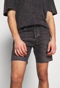 Black denim shorts with a frayed hem, straight cut, and subtle texture. Paired with an oversized, dark gray, short-sleeve t-shirt.