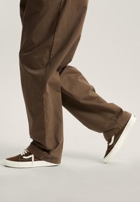 Brown pants with a relaxed fit and a textured surface, paired with brown sneakers featuring white accents and laces.