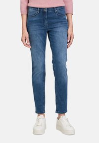 Modré džíny z denimu s úzkým střihem, designem s pěti kapsami a mírně vybledlým povrchem. Spárovány s bílými sportovními botami.
