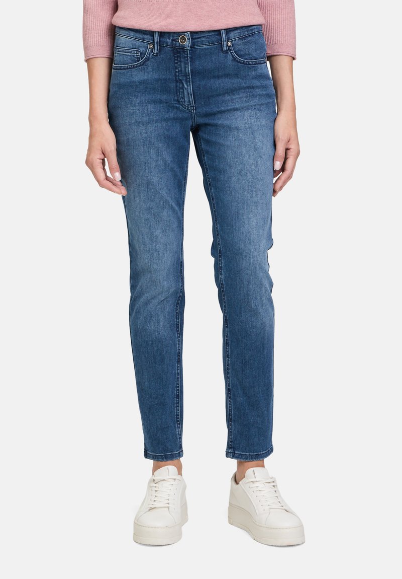 Modré džíny z denimu s úzkým střihem, designem s pěti kapsami a mírně vybledlým povrchem. Spárovány s bílými sportovními botami.