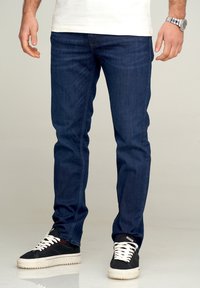 Mörkblå denimjeans med smal passform. Har klassisk sömnad och design med fem fickor. Kombinerade med svartvita sneakers.