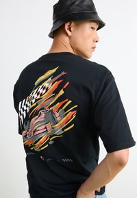 Black cotton t-shirt featuring a colorful graphic of a race car with motion lines and a checkered flag on the back. Short sleeves, relaxed fit.