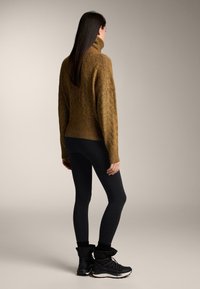 Pull en tricot marron avec un col haut, associé à des leggings noirs et des bottes noires. Tissu texturé et coupe décontractée.