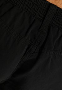 Detailní záběr na černou tkaninu s elastickým pasem a prošitými švy na oděvu.