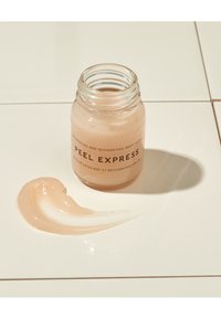 Glazen pot met een doorschijnende, lichtroze gelmasker met het label "Peel Express," met een gladde textuur, staat naast een swirls van het masker.