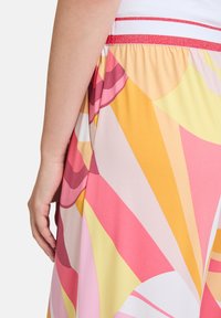 Kolorowe, wzorzyste spodnie z dużym różowym, żółtym i pomarańczowym wzorem. Posiadają białą elastyczną talię z czerwoną metaliczną paskiem.