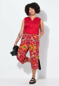 Top rosso senza maniche con scollo a V, abbinato a pantaloni rossi vivaci e stampati con design geometrici, motivi animali e una vestibilità comoda.