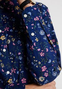 Floral button-up shirt featuring a dark blue background with small, colorful flowers. Has a classic collar and white buttons with a relaxed fit.