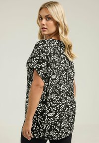 Czarna bluzka z białym abstrakcyjnym wzorem, z krótkim rękawem, okrągłym dekoltem i lekko zaokrąglonym dołem. Wykonana z lekkiego materiału.