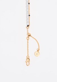 Collier en or avec des accents de perles transparentes et noires. Comprend un fermoir et un charme rond avec un détail en strass.