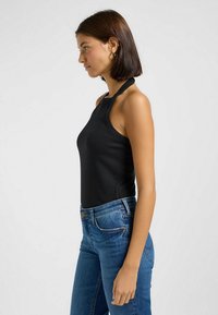 Svart ribbad halter top med en figurnära design, i kombination med blå denimjeans. Tyget är slätt och silhuetten är strömlinjeformad.
