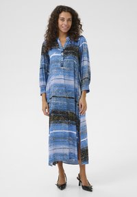 Maxi obleka z modro in črno vzorcem, z gumbnim izrezom, dolgimi rokavi in stranskim razporkom. Material ima gladko, tekočo teksturo.