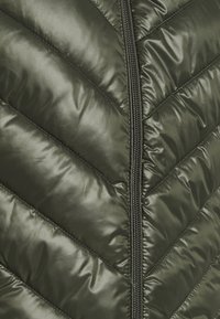 Nahaufnahme eines dunkelgrünen, gesteppte Stoffs mit diagonalen Nähten und einem schwarzen Reißverschluss in der Mitte.