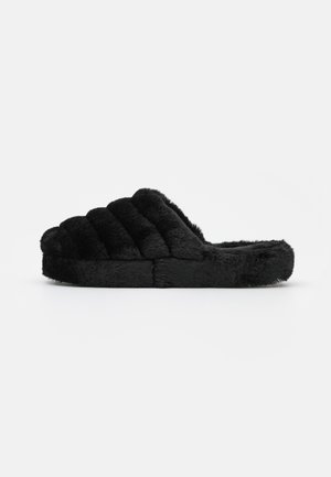 Chaussons en fourrure noire avec un design matelassé, bout ouvert, matériau textile doux et semelle plate. L'extérieur présente une texture moelleuse.