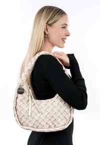 Geweven crèmekleurige handtas met een gebogen vorm en een textuur oppervlak. Voorzien van een ritssluiting en een decoratief label met een zilveren accent.