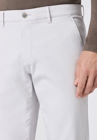 I pantaloni di cotone grigio chiaro presentano una vestibilità slim, tasche frontali e una chiusura con bottone. Il tessuto ha una texture liscia.