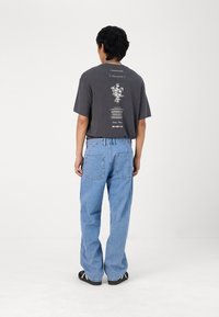 Grå kortermet t-skjorte med blomstertrykk og tekst på ryggen, kombinert med lyseblå jeans med rett ben og svarte sandaler.