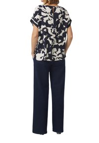 Marinebluse mit floralem Muster, kurzen Ärmeln und einem Schlüsselhole-Detail hinten, getragen mit weit geschnittenen, dunkelblauen Jeans, die eine lässige Outfit-Kombination zeigt.