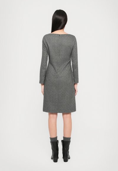 Un vestito grigio a maniche lunghe con una silhouette dritta, tessuto strutturato e dettaglio della zip sul retro, abbinato a stivaletti neri alla caviglia e polsini lavorati a maglia.