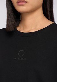 Svart sweatshirt med rund halsringning, med en matt Trussardi-logotyp på bröstet. Tyget känns slätt och har en medeltjocklek.