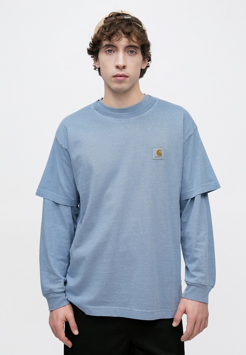 T-shirt bleu à manches courtes superposé à un haut à manches longues. Tissu en coton avec un col rond, présentant un petit écusson logo sur la poitrine.