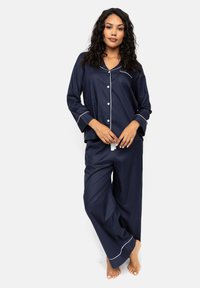 Navyblauw pyjamaset van zachte stof, met een knoopsluiting aan de bovenkant met lange mouwen en een ingezette zak, en losvallende broek met witte piping-accenten.