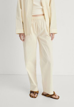Light yellow, loose-fitting cotton pants with an elastic waistband, paired with brown and tan striped flip-flops.