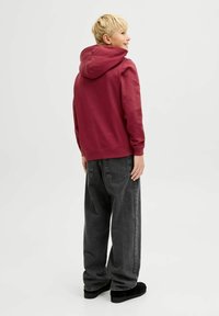 Sudadera con capucha color burdeos de corte relajado, combinada con unos pantalones vaqueros negros de corte holgado. La textura es suave. Footwear negro completa el conjunto.