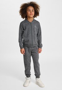 Grauer Reißverschluss-Sweatshirt mit passenden Jogginghosen, gerippten Bündchen und Bund. Geschichteter, strukturierter Stoff, ergänzt durch weiße Sneaker.
