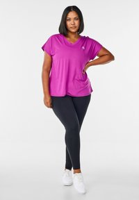Pink short-sleeve V-neck top, black leggings, white sneakers. Smooth fabric, relaxed fit, slight sheen on shirt, no visible patterns or hardware.
