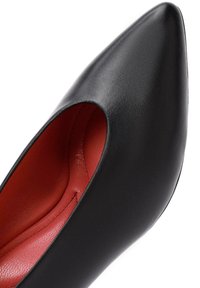 Scarpa nera in pelle con tacco alto, punta affusolata e design con ritagli. Interno foderato di un rosso vivace con una texture liscia.