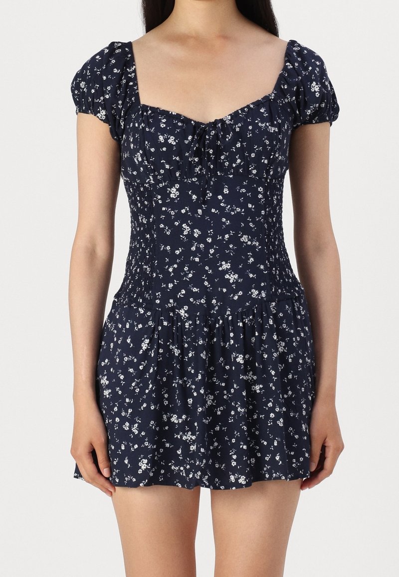 Námořnické květinové šaty s krátkými nabíranými rukávy, zpevněným živůtkem, čtvercovým výstřihem a rozšířenou sukní s bílými květinovými vzory.