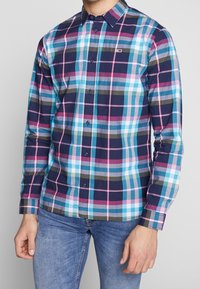 Chemise à manches longues à carreaux dans des couleurs marine, rose et aqua ; présente un col à bouton et des détails de bouton contrastants.