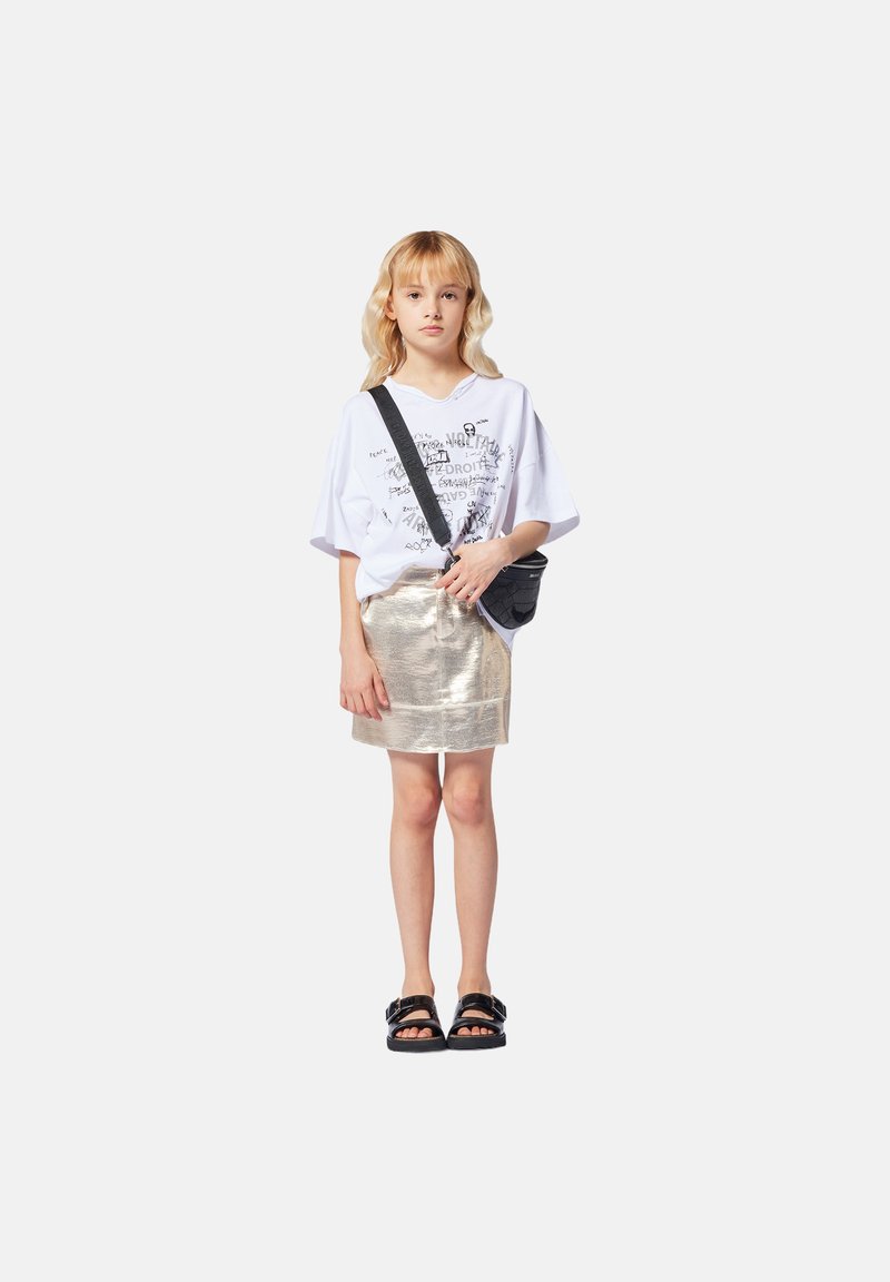 Witte oversized t-shirt met grafische print, metallic gouden minirok, zwarte schoudertas en zwarte sandalen met dikke straps.