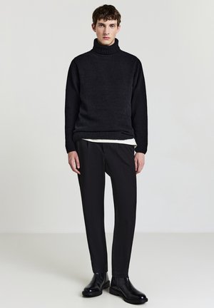 Schwarzer gestrickter Rollkragenpullover, strukturierter Stoff, kombiniert mit engen schwarzen Hosen und schwarzen Ankle Boots. Sauberes und minimalistisches Design.