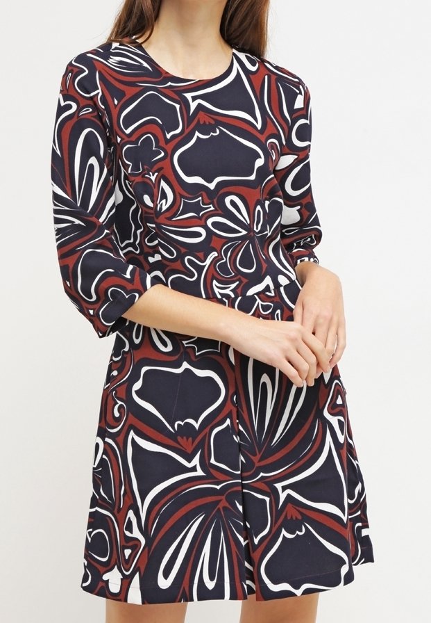 Femme portant une robe à manches longues avec des motifs floraux et géométriques abstraits en rouge, noir et blanc.