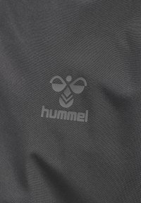 Schwarzer Stoff mit glatter Textur, der ein auffälliges graues Hummel-Logo-Design in der Mitte zeigt. Schlichte und minimalistische Erscheinung.