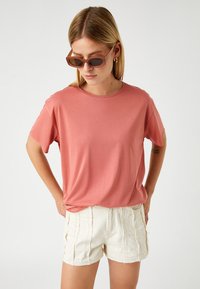 Rosa, kortærmet t-shirt lavet af blødt stof. Parret med lyse, strukturerede shorts. Accessories inkluderer solbriller.