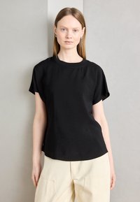 Haut noir à manches courtes avec une coupe décontract�ée et un col rond. Tissu texturé avec un léger éclat, associé à un pantalon couleur crème.