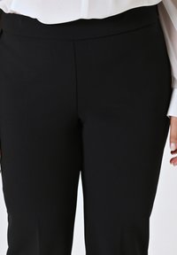 Pantaloni neri aderenti con una texture liscia e una vita a metà altezza. Presentano linee pulite e un design classico.