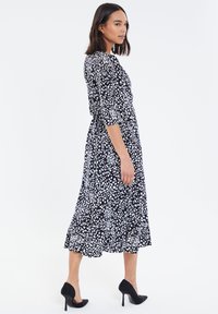 Vestido midi a lunares en blanco y negro con mangas tres cuartos, cintura elástica y dobladillo con volantes; combinado con zapatos de tacón alto negros.